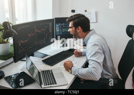 Je suis un gagnant heureux jeune trader en soirée et les lunettes en criant et se sentir heureux tout en regardant les graphiques commerciaux et des données financières dans le bureau. Stock Exchange. Concept de transactions financières. Concept d'investissement. Le marché de Forex Banque D'Images