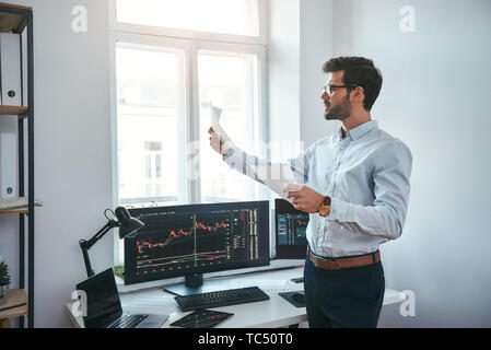 Stratégie de trading. Smart et les jeunes négociant de lunettes à la recherche de rapports financiers et l'analyse de graphiques commerciaux alors qu'il se tenait devant l'écran de l'ordinateur dans un bureau moderne. Courtier en valeurs. Le marché de Forex. Concept commercial Banque D'Images