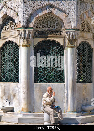 Istanbul, Turquie - 05/24/2010 : Les mauvais gras sur l'homme barbu en siège, à Yeni Cami (nouvelle mosquée) cour intérieure, en face de la construction de l'architecture Banque D'Images