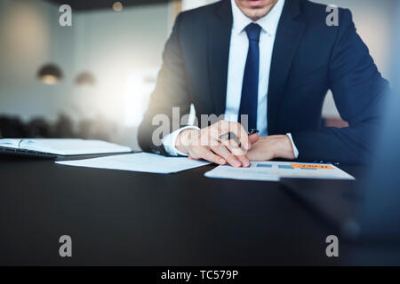 Closeup of a businessman looking at charts en allant sur la paperasse à son bureau dans un bureau moderne et lumineux Banque D'Images