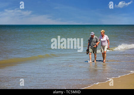 Heureux couple âgé pagayer dans l'eau de mer peu profonde sur une plage de sable le long de la côte en été Banque D'Images