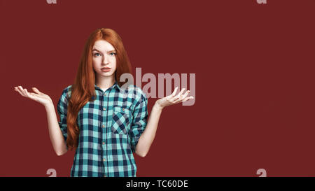 Cute girl rousse en chemise à carreaux vomit sa mains, isolé sur fond rouge Banque D'Images