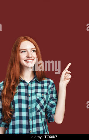 Close up of attractive ginger girl à chemise à carreaux, en soulignant bien qu'à côté, posant sur fond rouge. Shot verticale Banque D'Images