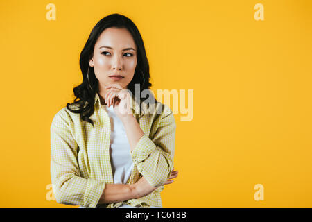 Pensive brunette fille asiatique isolé sur le jaune Banque D'Images