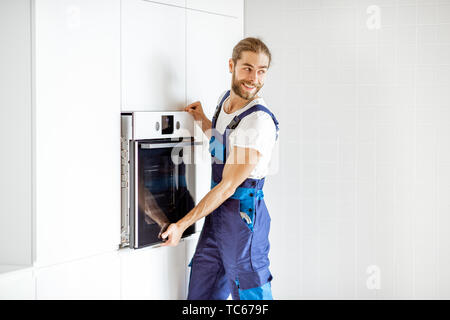 Beau workman en vêtements de l'installation d'un four électrique dans les étagères de cuisine à la cuisine moderne à la maison Banque D'Images