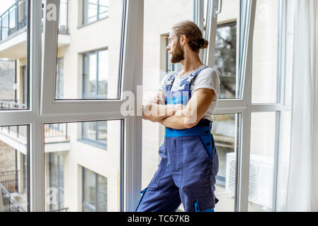 Portrait of a handsome workman en salopette, debout près de la fenêtre dans le renovared vacances Banque D'Images