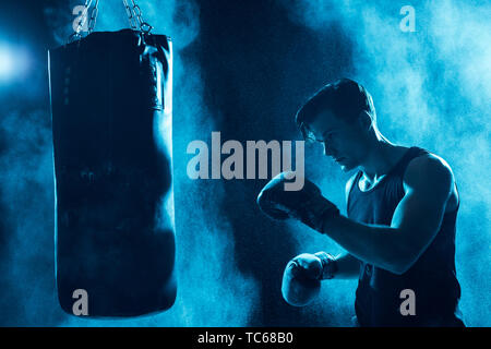 Boxer concentré dans des gants de boxe entraînement avec sac de boxe dans le noir Banque D'Images