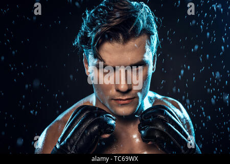 Vue avant du boxer dans les gants de cuir sous les gouttes d'eau sur noir Banque D'Images