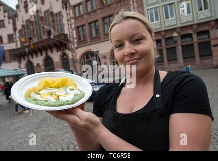 06 juin 2019, Hessen, Frankfurt/Main : une femme sur le Römerberg présente une plaque avec une sauce verte 'classique'. Une tentative de record du monde s'exécute dans la métropole principale jusqu'au soir, où au moins 231 771 doit être mangé. Photo : Boris Roessler/dpa Banque D'Images