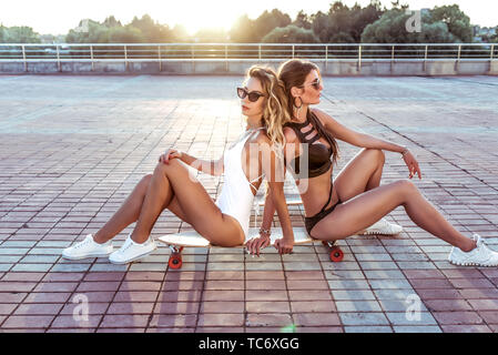 Deux jeunes filles amies siéger skateboard vous détendre bronzer, summer city, skate boards, longboard maillot de bain. Le modèle de mode, style de vie moderne. Idée Concept Banque D'Images