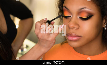 L'artiste de maquillage Mascara cils applique à de petite fille africaine. Maquillage de soirée. Closeup portrait Banque D'Images