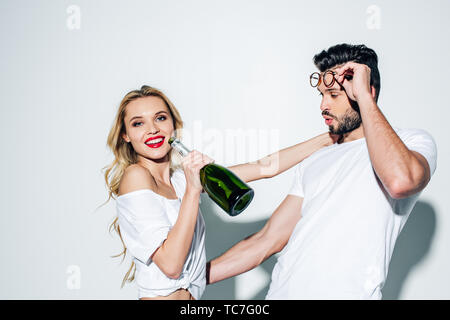 Cheerful blonde girl holding bouteille de champagne près de bel homme, dans les verres sur blanc Banque D'Images