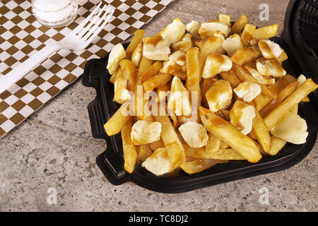 La poutine dans un récipient pour emporter. Cuite avec des frites, de la sauce et du fromage. Une cuisine canadienne. Banque D'Images