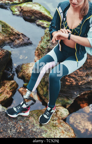 La vérification des résultats. Photo recadrée de la femme athlète handicapée dans les vêtements de sport avec prothèse contrôler podomètre, assis sur la pierre. Mobilité sportif. Mode de vie sain. Sport concept Banque D'Images