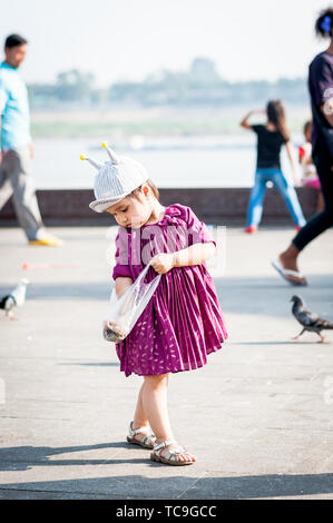 Une jolie petite fille alimente joyeusement les pigeons le long de la promenade de Phnom Penh, au Cambodge. Banque D'Images