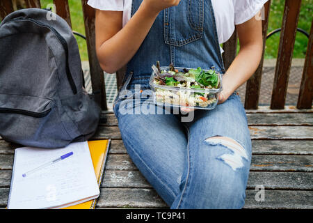 Portrait Portrait d'un élève fille assise dans un banc en mangeant salade saine avec des pâtes de verre dans une boîte à lunch Banque D'Images