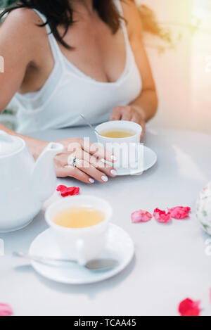 Verres et woman's hands holding une tasse sur la table avec des pétales de rose, vue d'en haut. Banque D'Images