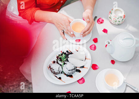 Verres et woman's hands holding une tasse sur la table avec des pétales de rose, vue d'en haut. Banque D'Images