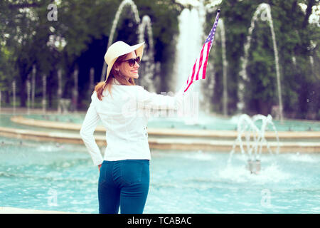 Patriot woman in hat holding USA flag en parc à fontaine, vue arrière, le jour de l'indépendance, 4 juillet, style vintage Banque D'Images