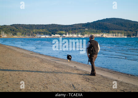 Puntone Scarlino, Maremme Toscane, Italie - circa 2019 Avril - Fisherman marche sur la plage avec son chien au coucher du soleil Banque D'Images