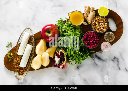 Ingrédients pour la cuisson la Grenade et poires Salade verte avec vinaigrette au gingembre sur une planche en bois sur le marbre blanc Banque D'Images