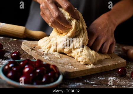 Libre d'un jeune homme de race blanche d'un morceau de pétrissage de pâte pour préparer une cireres de coca cherry, une galette sucrée typique de la Catalogne, en Espagne, sur un wo Banque D'Images