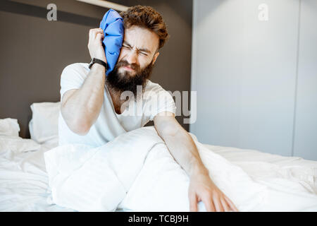 L'homme se sentir mal, assis sur le lit avec maux de tête et de l'application de sac de glace Banque D'Images