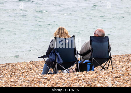 Un couple d'âge moyen s'assit sur les chaises ou chaises de camping sur une plage de galets de la mer Banque D'Images