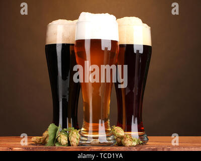 Trois verres de bières différentes et hop sur la table en bois sur fond brun Banque D'Images