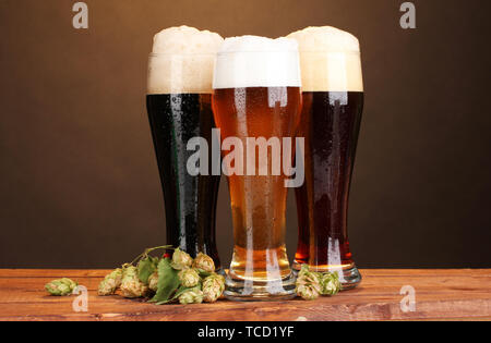 Trois verres de bières différentes et hop sur la table en bois sur fond brun Banque D'Images