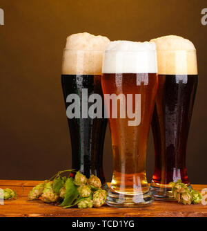 Trois verres de bières différentes et hop sur la table en bois sur fond brun Banque D'Images