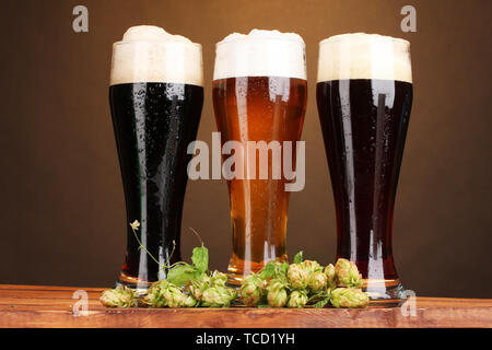 Trois verres de bières différentes et hop sur la table en bois sur fond brun Banque D'Images