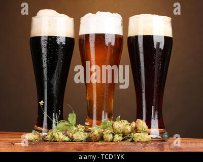 Trois verres de bières différentes et hop sur la table en bois sur fond brun Banque D'Images