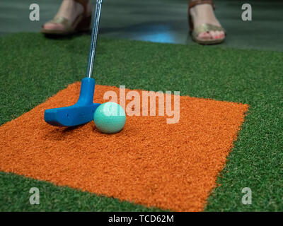 Putter bleu sur le gazon à côté de green balle de golf sur un golf miniature avec femme frapper Banque D'Images
