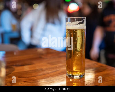 Tall skinny verre de bière lager dorée assis sur comptoir bar les gens en arrière-plan Banque D'Images