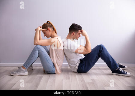 Triste jeune couple assis dos à dos sur le plancher à la maison Banque D'Images