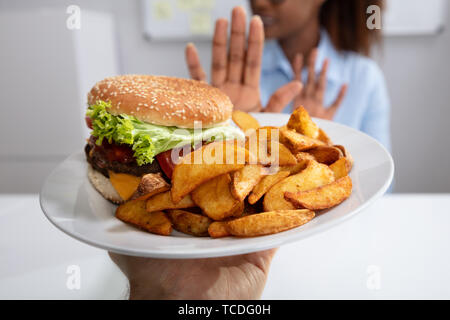 Jeune femme refusant burger et frites On Plate Banque D'Images