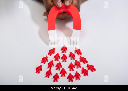 Close-up of a person's Hand Holding Red Horseshoe aimant qui attire des figures humaines rouge Banque D'Images