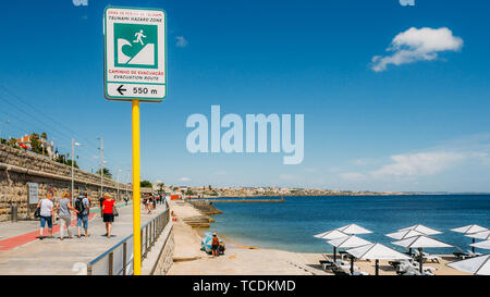 Cascais, Portugal - 5 juin 2019 : Tsunami evaculation signe route à côté d'une promenade en bord de mer avec les piétons à Cascais, Portugal Banque D'Images