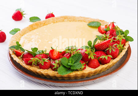 Tarte aux fraises et crème fouettée décoré de feuilles de menthe sur fond clair. Banque D'Images