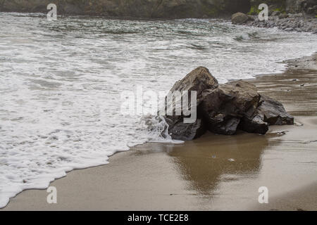 Paysage de la plage de sable humide avec rock et vague blanc avec mousse d'exécution sur la surface Banque D'Images