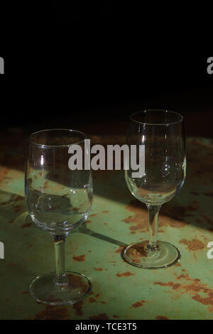 Deux verres de vin vide s'asseoir sur le dessus d'une table rustique vert rouillé. La lumière du soleil illumine la fenêtre de lunettes. Banque D'Images