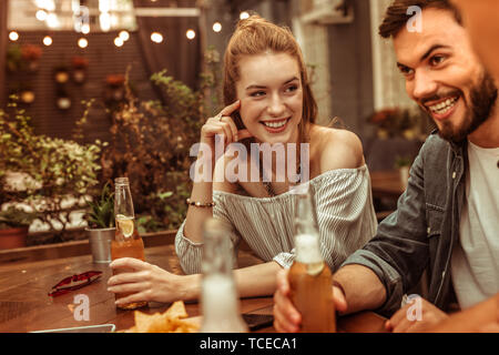 Un verre avec des amis. Soutenu heureux joyeux belle jeune femme rousse un verre avec vos amis au bar Banque D'Images