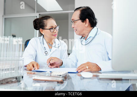 Asian cardiologues assis à table et discuter des patients cardiogramme Banque D'Images