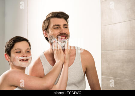 Preteen boy l'application de mousse à raser à sourire père dans la salle de bains Banque D'Images