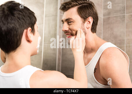 Preteen boy l'application de mousse à raser à sourire père dans la salle de bains Banque D'Images