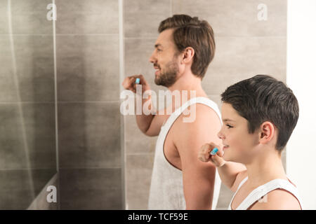 Smiling fils et papa se brosser les dents le matin dans la salle de bains Banque D'Images