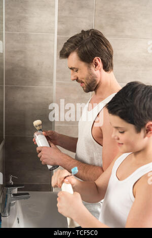 Fils se brosser les dents et papa dans le rasage Matin dans la salle de bains Banque D'Images