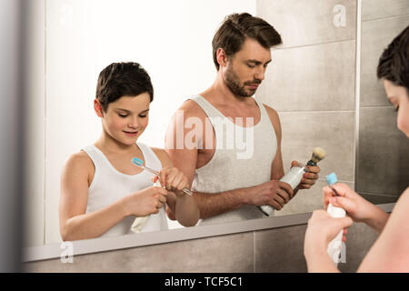 Fils se brosser les dents et papa dans le rasage Matin dans la salle de bains Banque D'Images