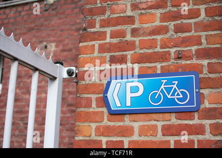 Parking vélo bleu brun rouge signe sur mur de briques à côté de clôture blanche. Banque D'Images